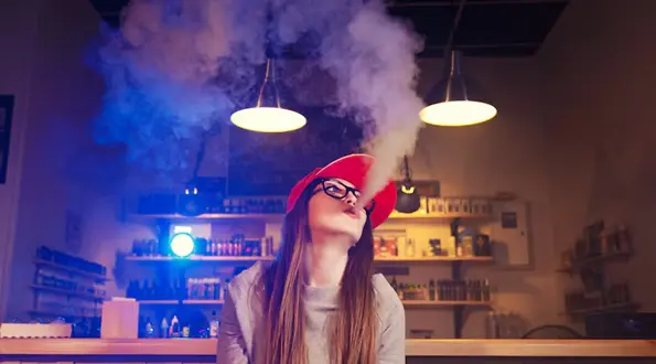 Person Exhaling Vapor Inside a Smoke Shop with Shelves of Products